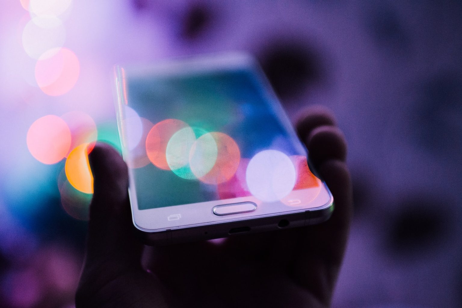Blurred smartphone screen reflecting colourful blue lights in a dimly lit setting