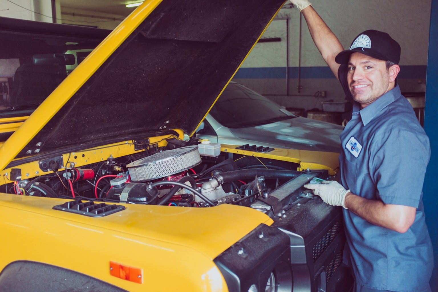 Mechanic smiling while working on a yellow car engine in a garage