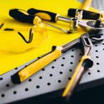 Yellow safety goggles and tools on a perforated metal surface in a workshop setting