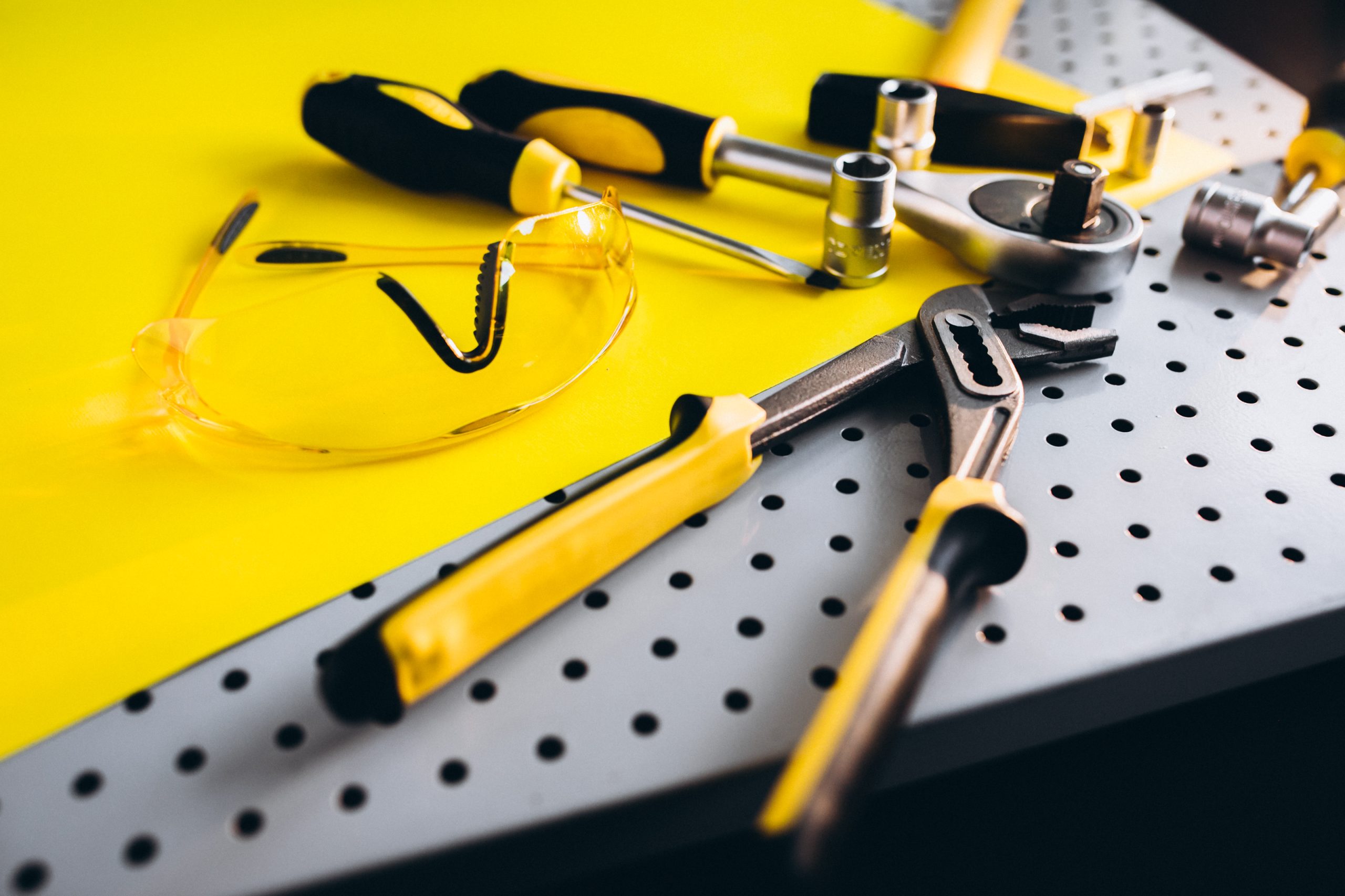 Yellow safety goggles and tools on a perforated metal surface in a workshop setting